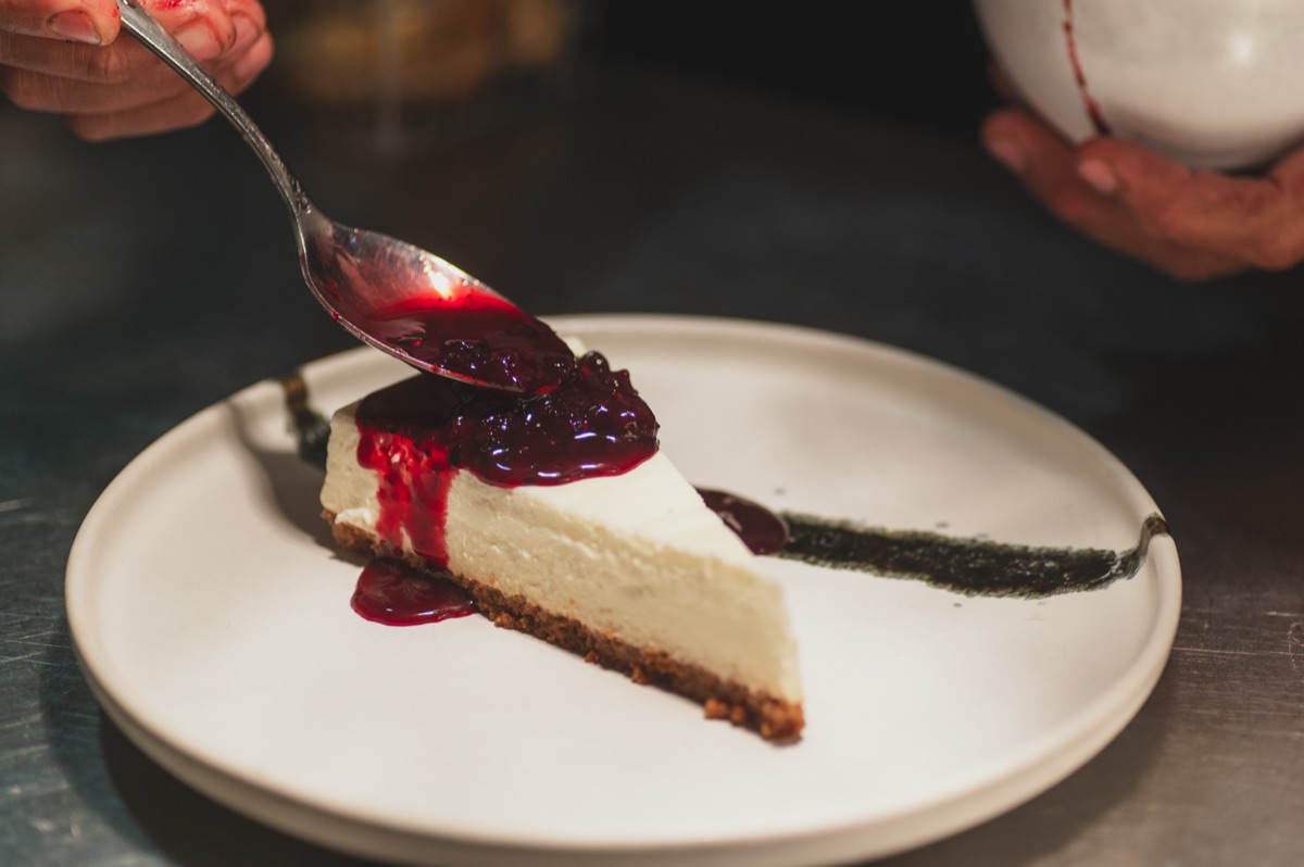 Cheesecake with berry sauce being spooned onto the plate